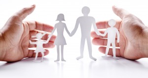 Cardboard figures of the family on a white background. The symbol of unity and happiness. Hands gently hug the family.